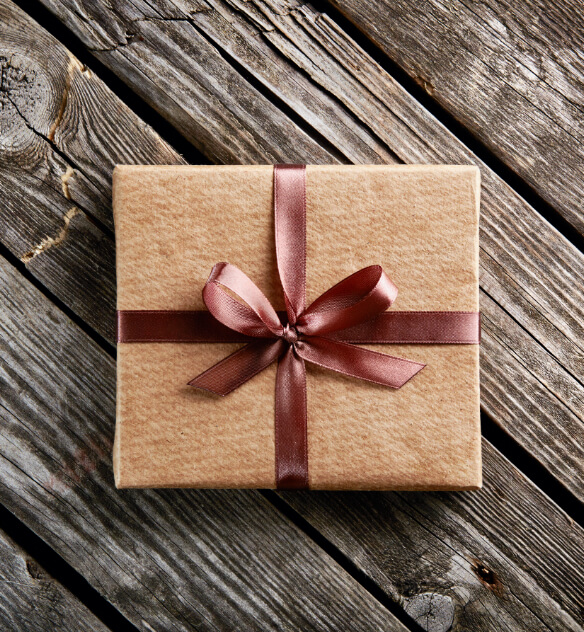 A brown package wrapped with dark red ribbon sitting on top of a wooden surface