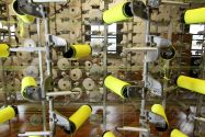 Several small rolls of yellow and white fabric being processed by a tall metal piece of machinery